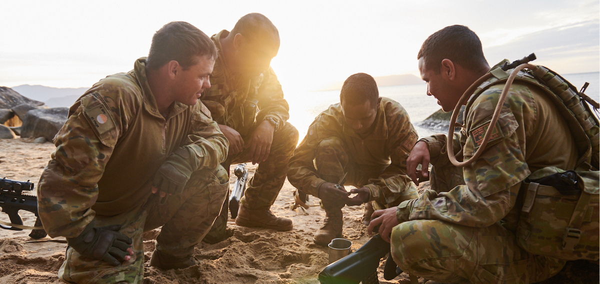 Soldiers in uniform kneeling on the beach, displaying unity and determination.