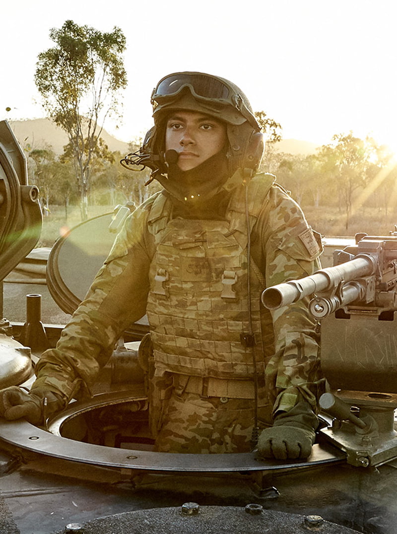 An Army member standing inside a tank, preparing for combat.