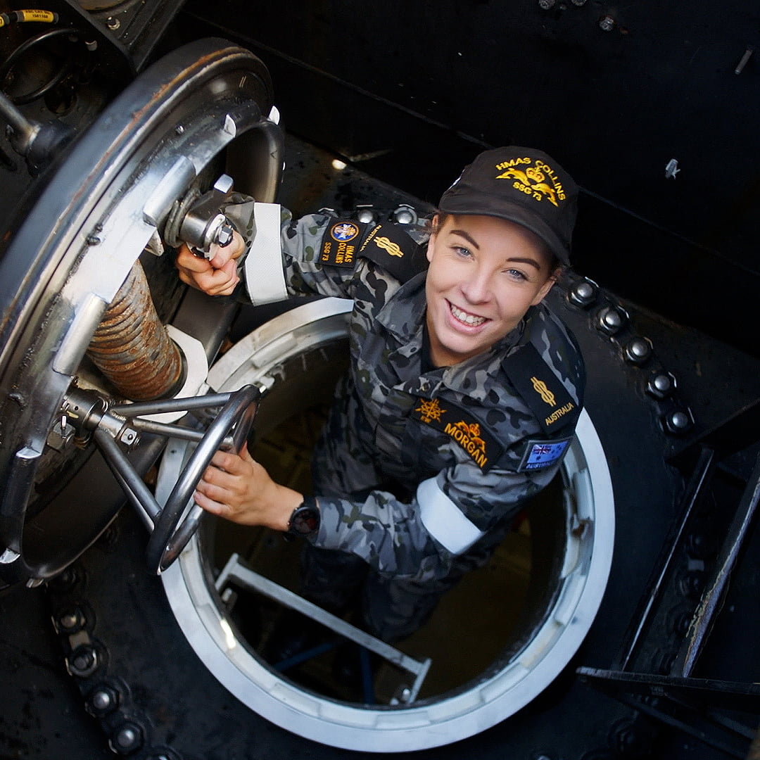 A Navy member climbing out of a submarine smiling.