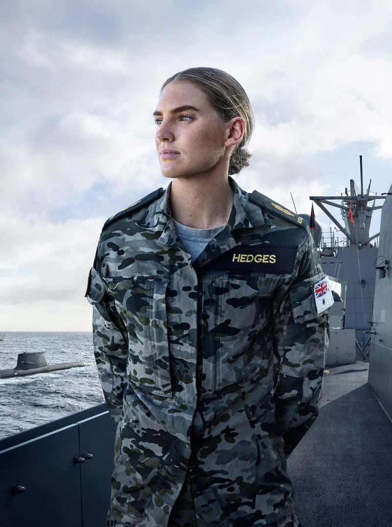 A woman in camouflage uniform standing on a ship, ready for action.