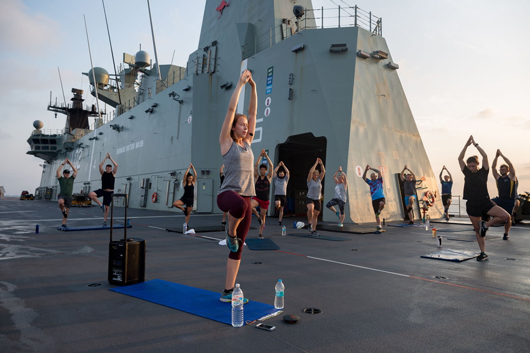 A group of people practicing yoga outside on top of a ship.