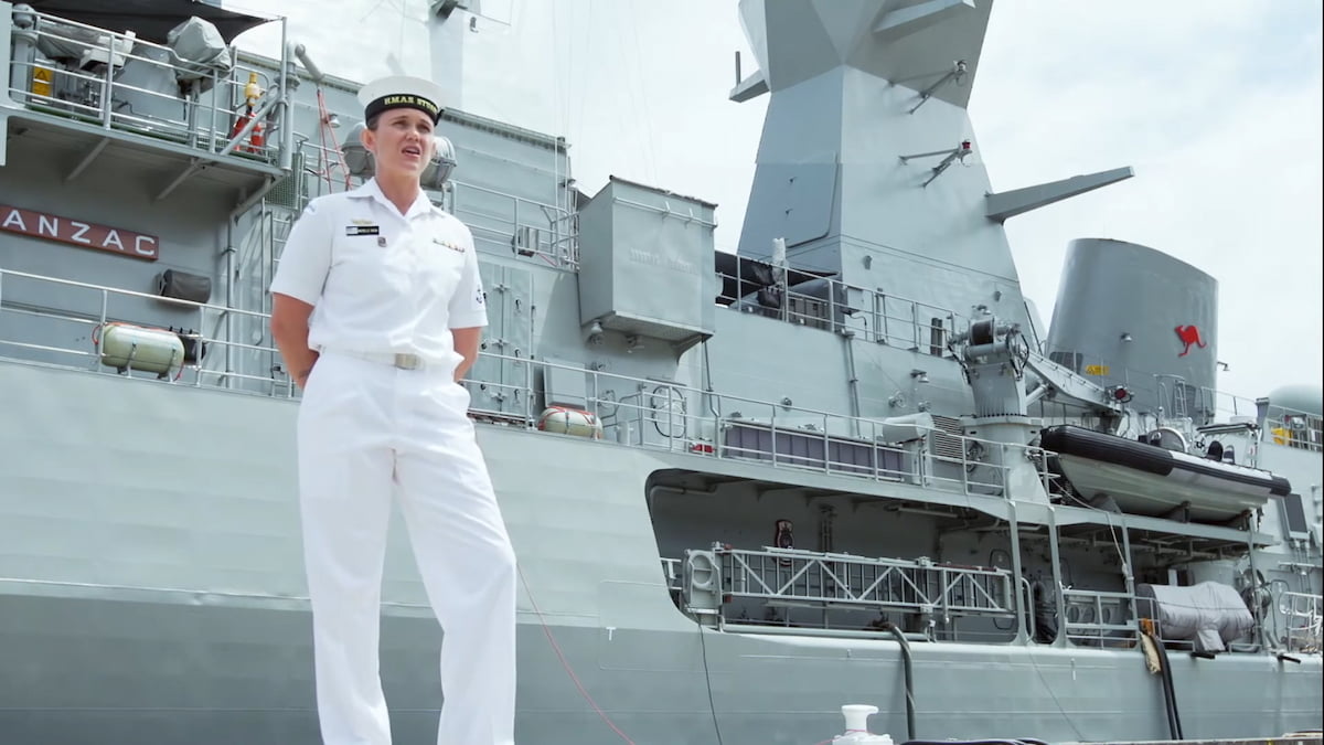 A woman in the Navy stands outside on a ship.