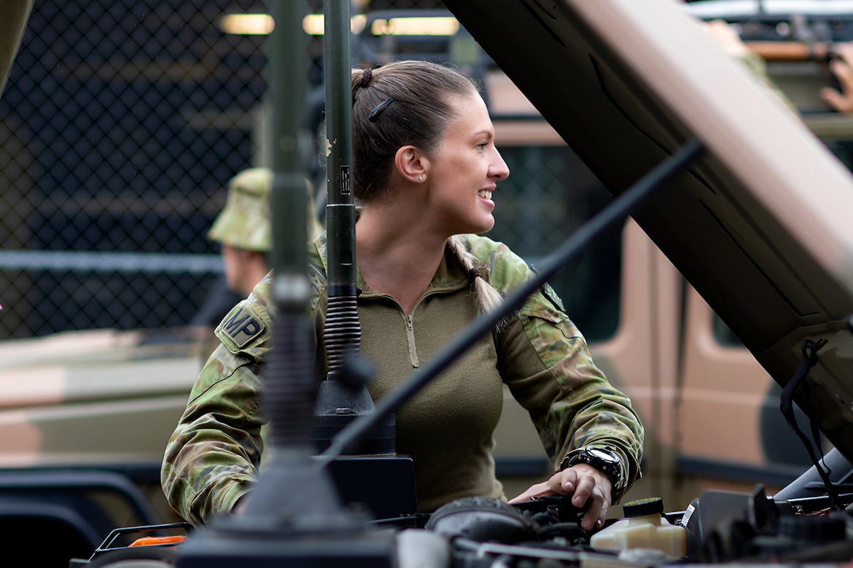 Military Policewoman Shannon is under the hood of an Army vehicle.Tara