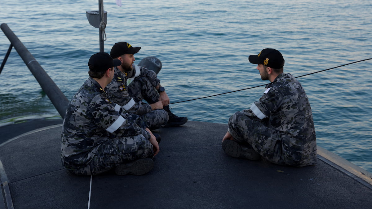 Three men in Navy uniforms sitting outside.