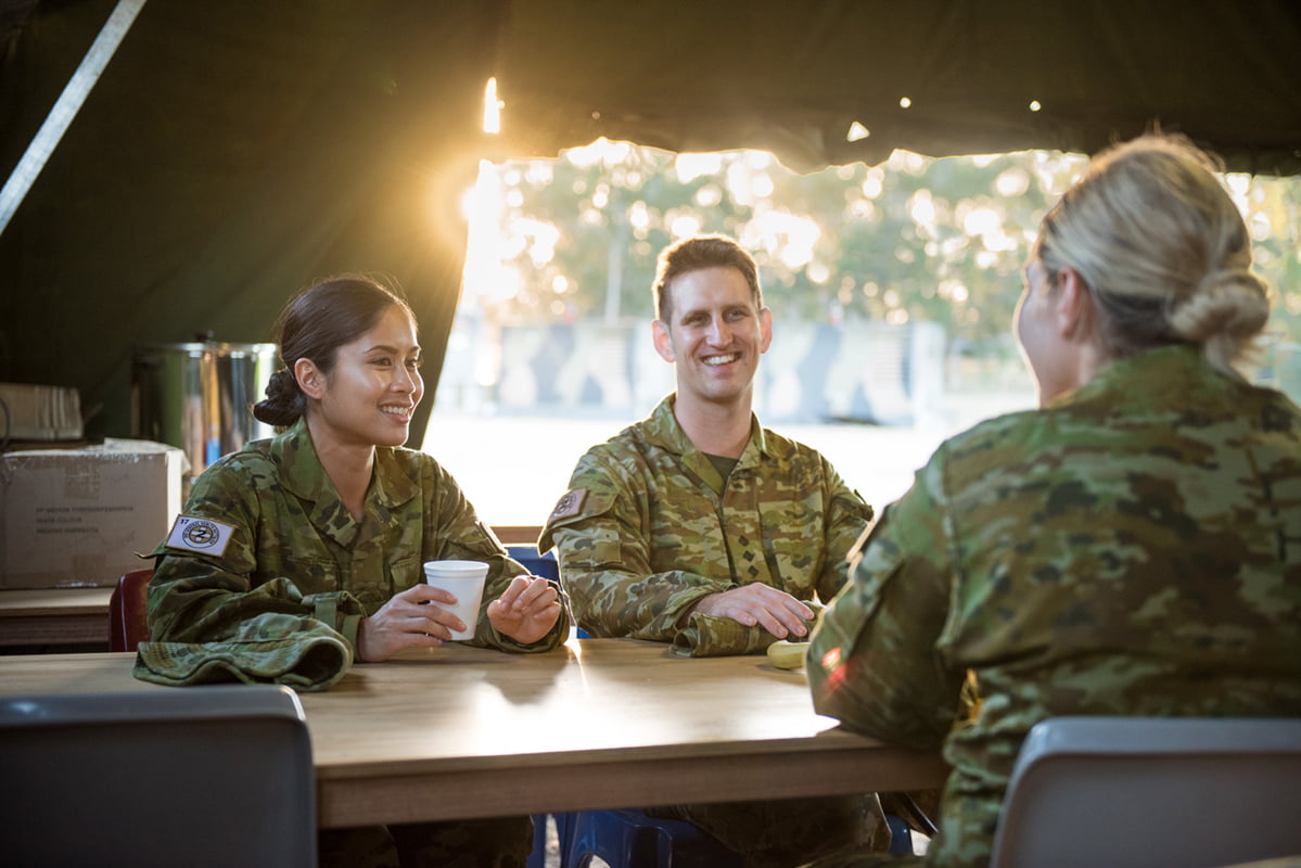 Three members of the Army sit at a table smiling.