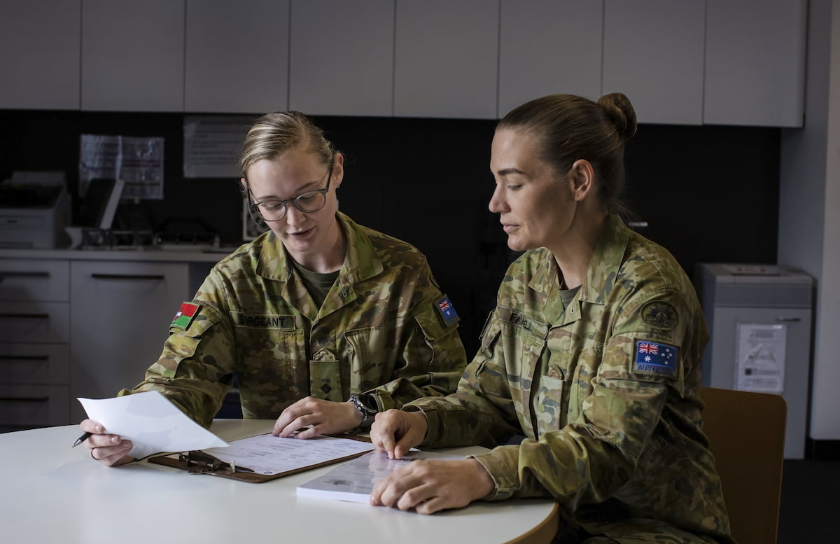 Two members of the Army review papers at a desk.