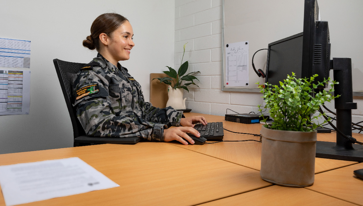 A member of the Navy sits contentedly at her computer between two ferns.