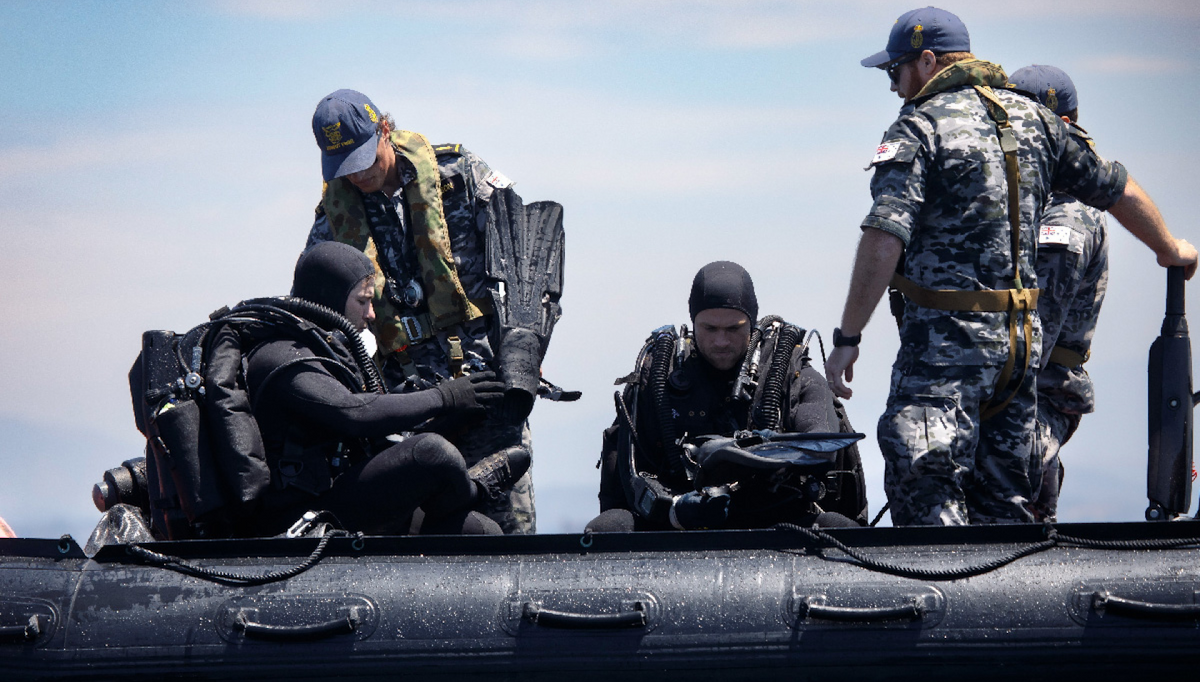Navy personnel emerge from a submarine hatch.