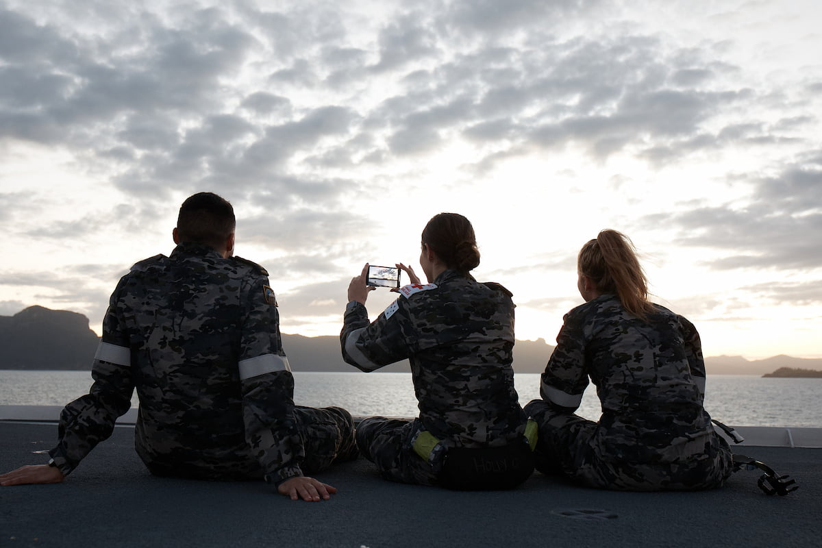 Three members of the Navy are outside looking at the sunset.