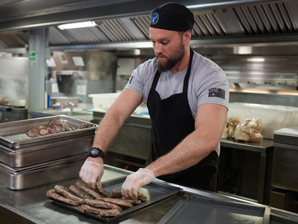 A male Navy chef preps meat in the galley.
