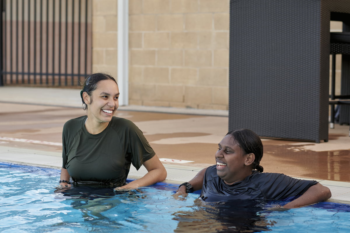 Two women stand in a pool smiling.