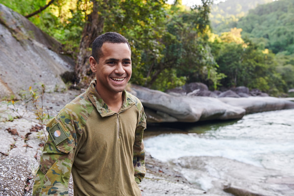 A young soldier in uniform standing by a river.