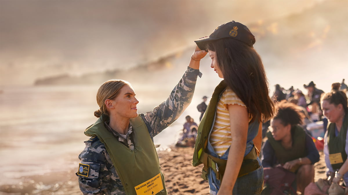 A woman in the Navy stands on the beach with a young girl.