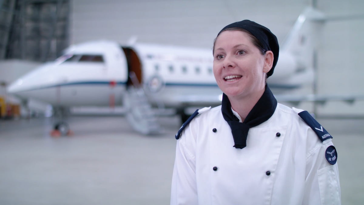 A woman in a chef uniform stands in front of an airplane.