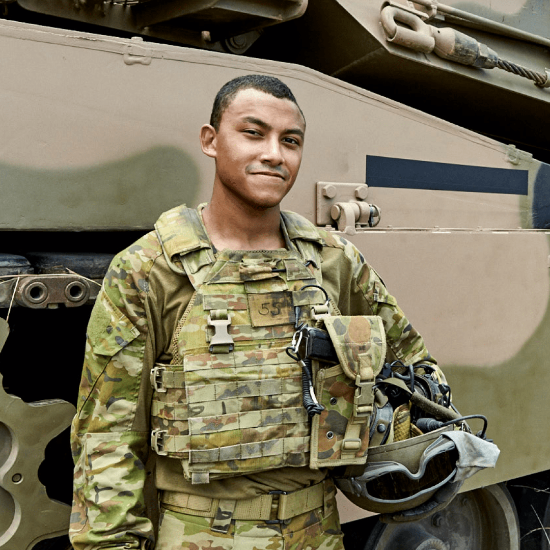 Armoured Vehicle Crew member Jeremy stands in front of an Army vehicle