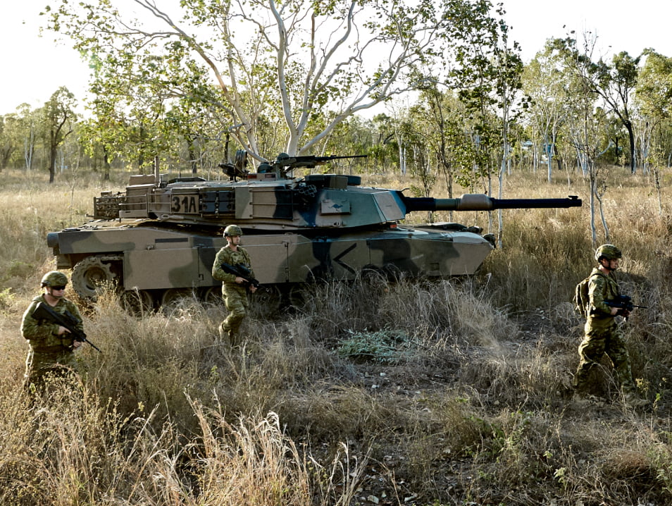 Members of the Australian walk through a field with a tank.