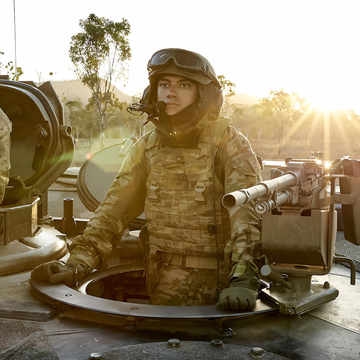 An Army member is standing inside a tank, preparing for combat.